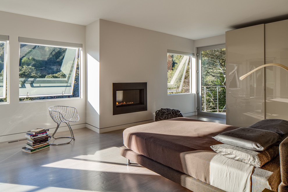 Large modern master bedroom in San Francisco with white walls, a ribbon fireplace, brown floor, medium hardwood floors and a metal fireplace surround.