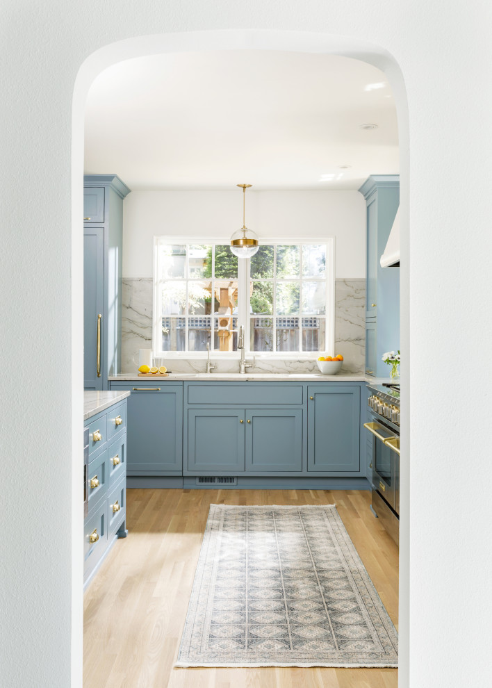 Klassisk inredning av ett mellanstort kök, med en undermonterad diskho, luckor med infälld panel, blå skåp, bänkskiva i kvartsit, stänkskydd i sten, integrerade vitvaror, ljust trägolv och en halv köksö