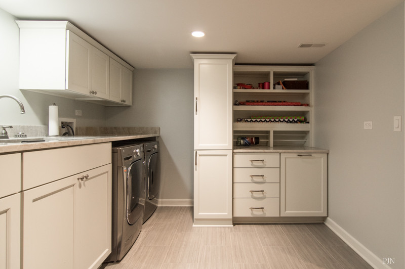 Photo of a mid-sized transitional single-wall utility room in Chicago with an undermount sink, recessed-panel cabinets, white cabinets, quartz benchtops, grey walls, porcelain floors and a side-by-side washer and dryer.
