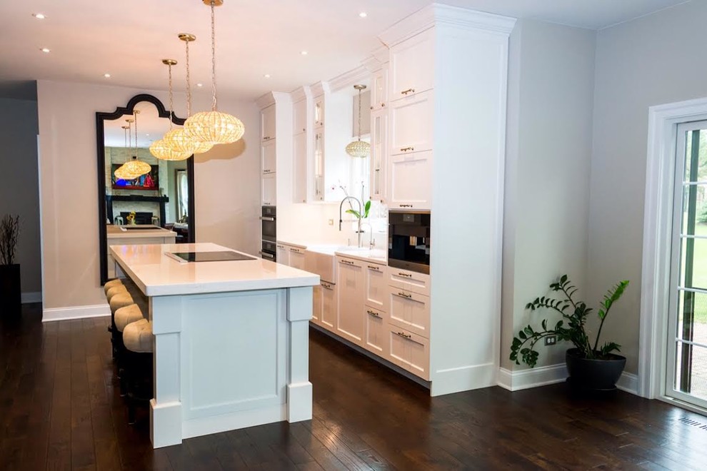 Example of a mid-sized transitional single-wall dark wood floor enclosed kitchen design with a farmhouse sink, shaker cabinets, white cabinets, white backsplash, stainless steel appliances and an island