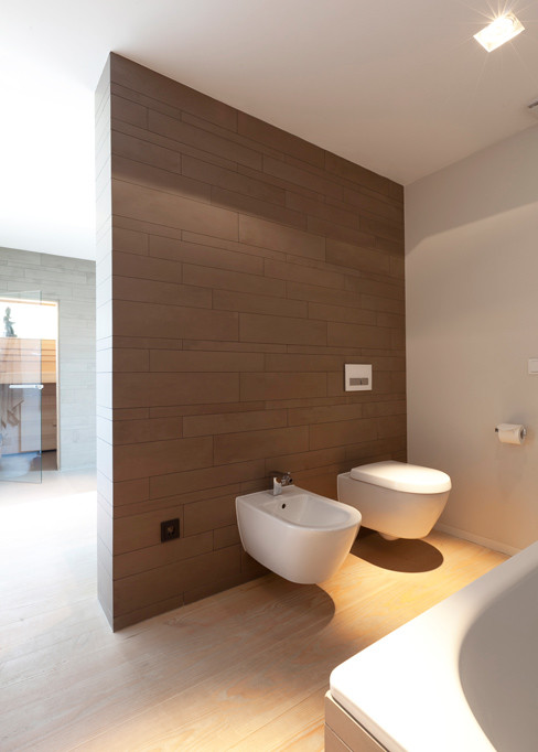 Inspiration for a mid-sized contemporary 3/4 bathroom in Frankfurt with glass-front cabinets, a drop-in tub, a curbless shower, a wall-mount toilet, beige tile, ceramic tile, beige walls, light hardwood floors, solid surface benchtops and an integrated sink.