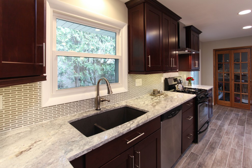 Example of a large transitional u-shaped porcelain tile eat-in kitchen design in Chicago with an undermount sink, recessed-panel cabinets, dark wood cabinets, granite countertops, gray backsplash, glass tile backsplash, stainless steel appliances and an island
