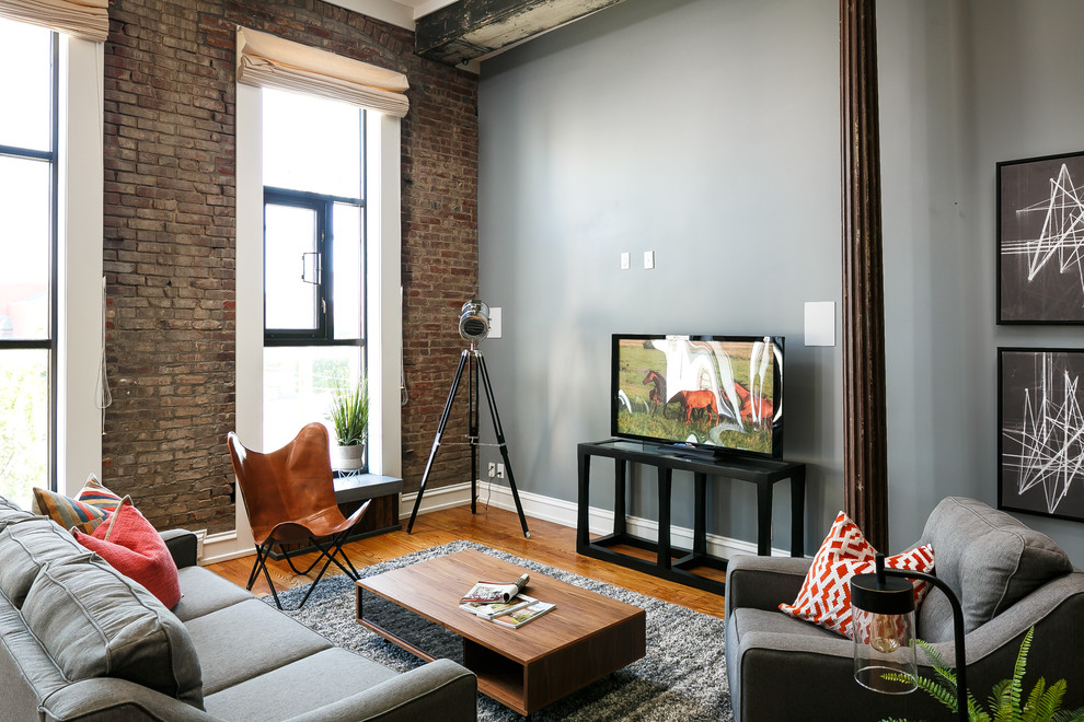 This is an example of an industrial open concept family room in Louisville with grey walls, medium hardwood floors, no fireplace and a freestanding tv.