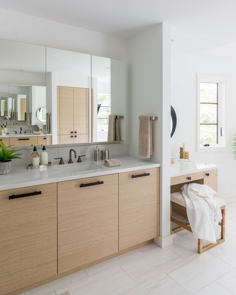 This is an example of a large contemporary master bathroom in New York with flat-panel cabinets, light wood cabinets, a freestanding tub, a corner shower, white walls, white floor, a hinged shower door, white benchtops, limestone benchtops, limestone floors and an undermount sink.