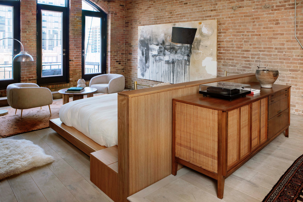 Inspiration for a contemporary master bedroom in Chicago with light hardwood floors, a standard fireplace, a plaster fireplace surround, beige floor, exposed beam, brick walls and brown walls.