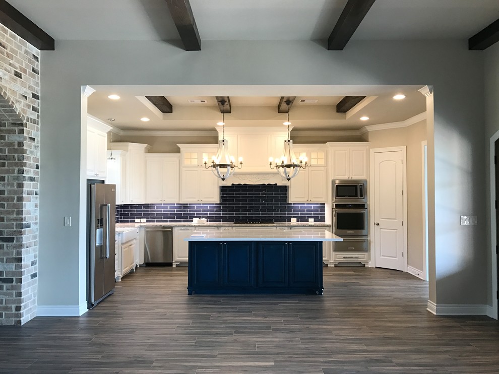 Open concept kitchen - large transitional l-shaped laminate floor and gray floor open concept kitchen idea in Austin with a farmhouse sink, raised-panel cabinets, white cabinets, quartzite countertops, blue backsplash, subway tile backsplash, stainless steel appliances, an island and white countertops
