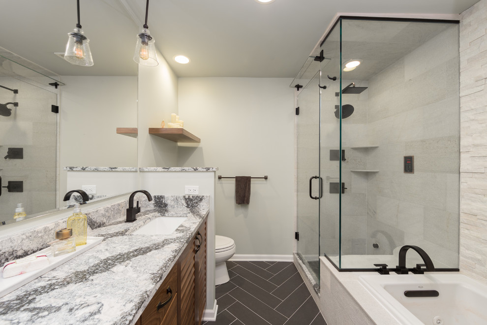 This is an example of a mid-sized contemporary master bathroom in Chicago with flat-panel cabinets, medium wood cabinets, a drop-in tub, an alcove shower, a one-piece toilet, beige walls, cement tiles, an undermount sink, limestone benchtops, beige tile and travertine.