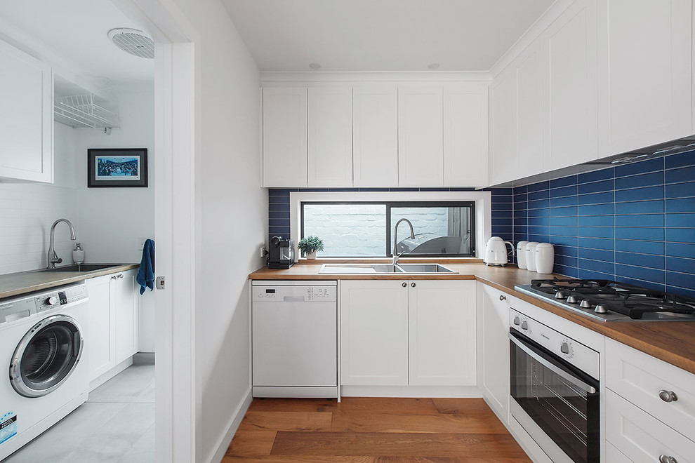 Contemporary l-shaped kitchen in Melbourne with a drop-in sink, shaker cabinets, white cabinets, wood benchtops, blue splashback, white appliances, medium hardwood floors, brown floor and brown benchtop.