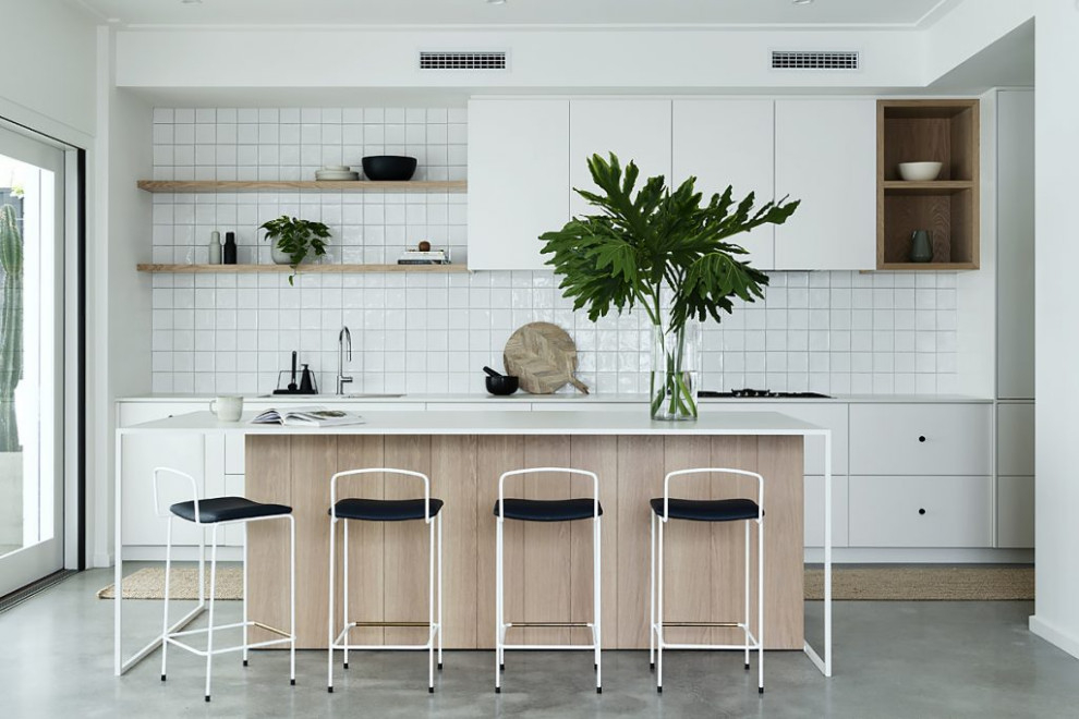 This is an example of a beach style galley kitchen in Perth with an undermount sink, flat-panel cabinets, white cabinets, white splashback, concrete floors, with island, grey floor and white benchtop.