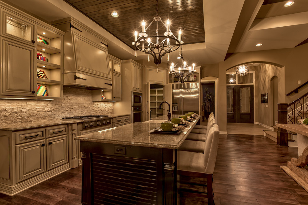 Design ideas for a mid-sized country l-shaped open plan kitchen in Omaha with a farmhouse sink, raised-panel cabinets, beige cabinets, quartzite benchtops, beige splashback, stone tile splashback, stainless steel appliances, dark hardwood floors, with island and brown floor.