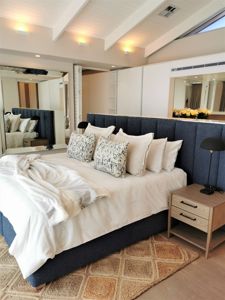 This is an example of a large beach style master bedroom with white walls, no fireplace, brown floor and exposed beam.