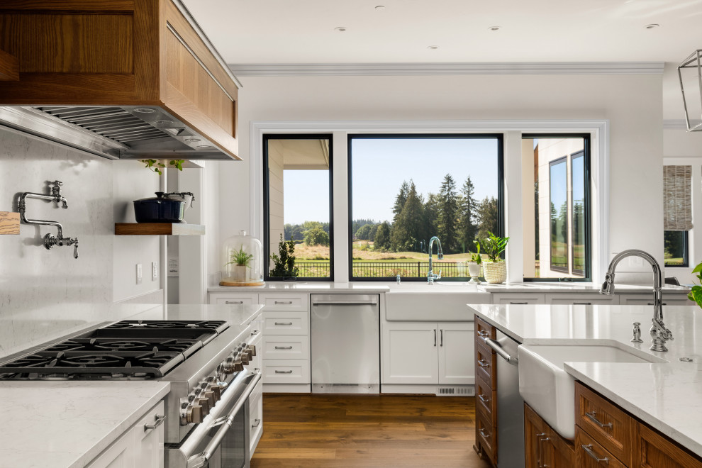 Inspiration for a mid-sized country l-shaped eat-in kitchen in Los Angeles with a farmhouse sink, medium wood cabinets, white splashback, stainless steel appliances, medium hardwood floors, with island, brown floor, white benchtop, shaker cabinets and stone slab splashback.