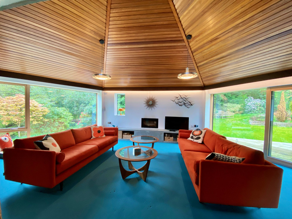 This is an example of a medium sized midcentury mezzanine living room with a home bar, white walls, carpet, a wood burning stove, a freestanding tv, blue floors and a timber clad ceiling.