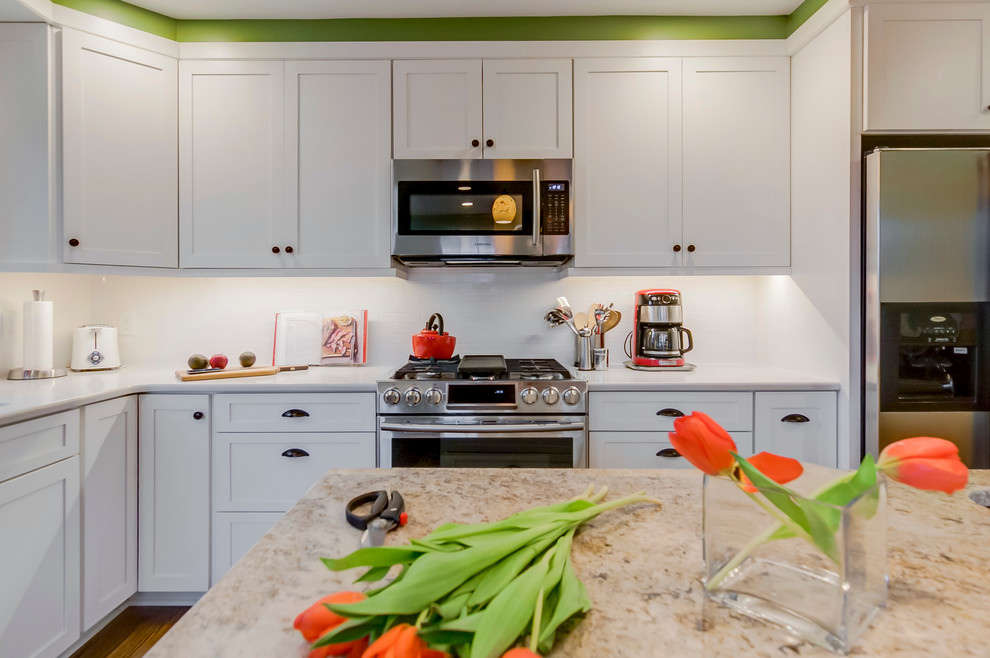 This is an example of a modern l-shaped eat-in kitchen in DC Metro with an undermount sink, white cabinets, white splashback, ceramic splashback, stainless steel appliances, light hardwood floors and with island.