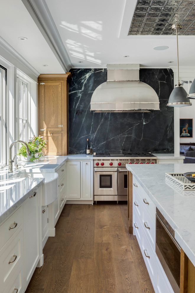 Kitchen - large traditional l-shaped medium tone wood floor and brown floor kitchen idea in Boston with a farmhouse sink, shaker cabinets, white cabinets, marble countertops, black backsplash, stone slab backsplash, stainless steel appliances, an island and white countertops