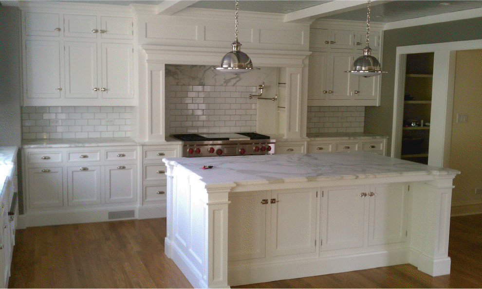 This is an example of a mid-sized traditional l-shaped open plan kitchen in Chicago with a farmhouse sink, recessed-panel cabinets, yellow cabinets, marble benchtops, white splashback, stone slab splashback, panelled appliances, light hardwood floors and multiple islands.