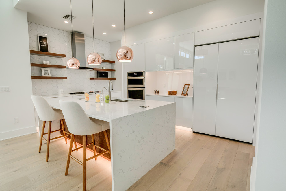 Mid-sized modern l-shaped eat-in kitchen in Tampa with a double-bowl sink, flat-panel cabinets, white cabinets, quartz benchtops, white splashback, ceramic splashback, stainless steel appliances, light hardwood floors, with island, beige floor and white benchtop.