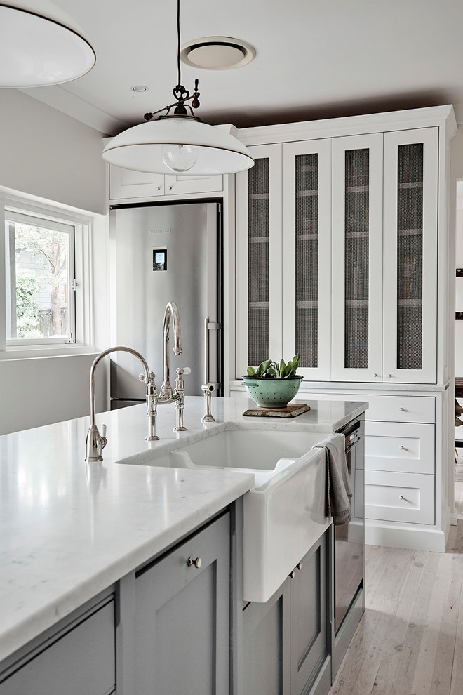 Photo of a mid-sized traditional u-shaped kitchen pantry in Sydney with a farmhouse sink, shaker cabinets, white cabinets, marble benchtops, white splashback, subway tile splashback, stainless steel appliances, light hardwood floors and with island.
