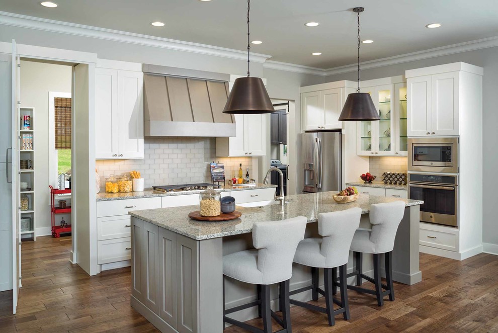 Beach style kitchen in Other with a farmhouse sink, shaker cabinets, white cabinets, granite benchtops, beige splashback, stainless steel appliances, with island, brown floor, subway tile splashback and dark hardwood floors.