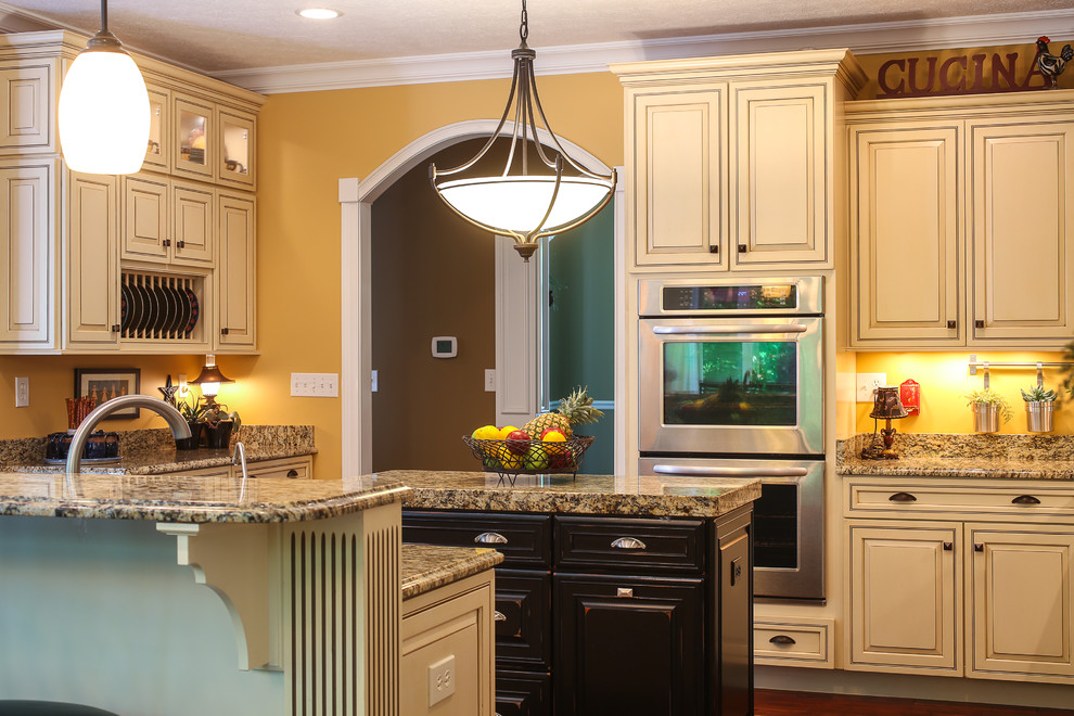 Example of a large transitional l-shaped dark wood floor enclosed kitchen design with a double-bowl sink, raised-panel cabinets, beige cabinets, granite countertops, yellow backsplash, stainless steel appliances and an island