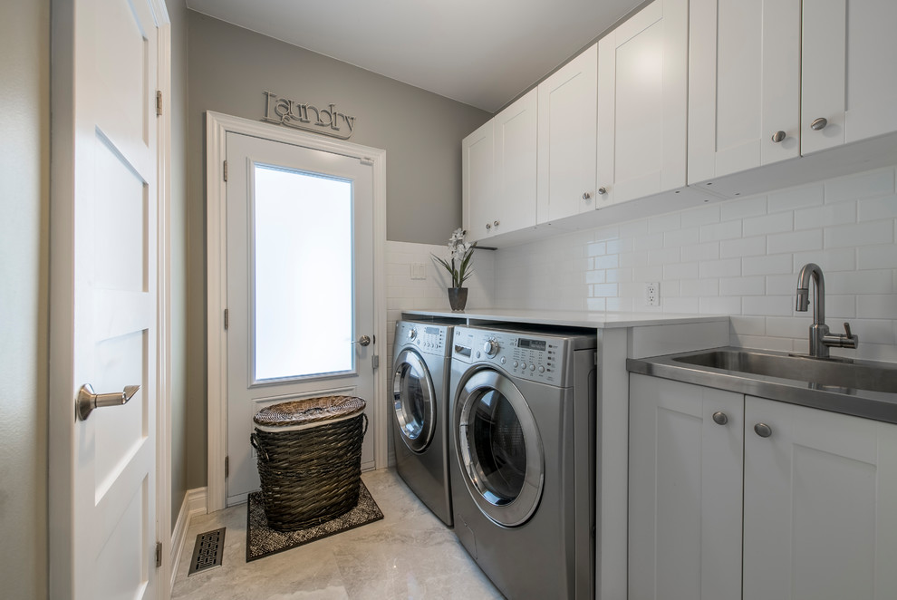 Photo of a mid-sized contemporary single-wall laundry room in Toronto with an integrated sink, shaker cabinets, white cabinets, solid surface benchtops, grey walls, a side-by-side washer and dryer, beige floor and white benchtop.