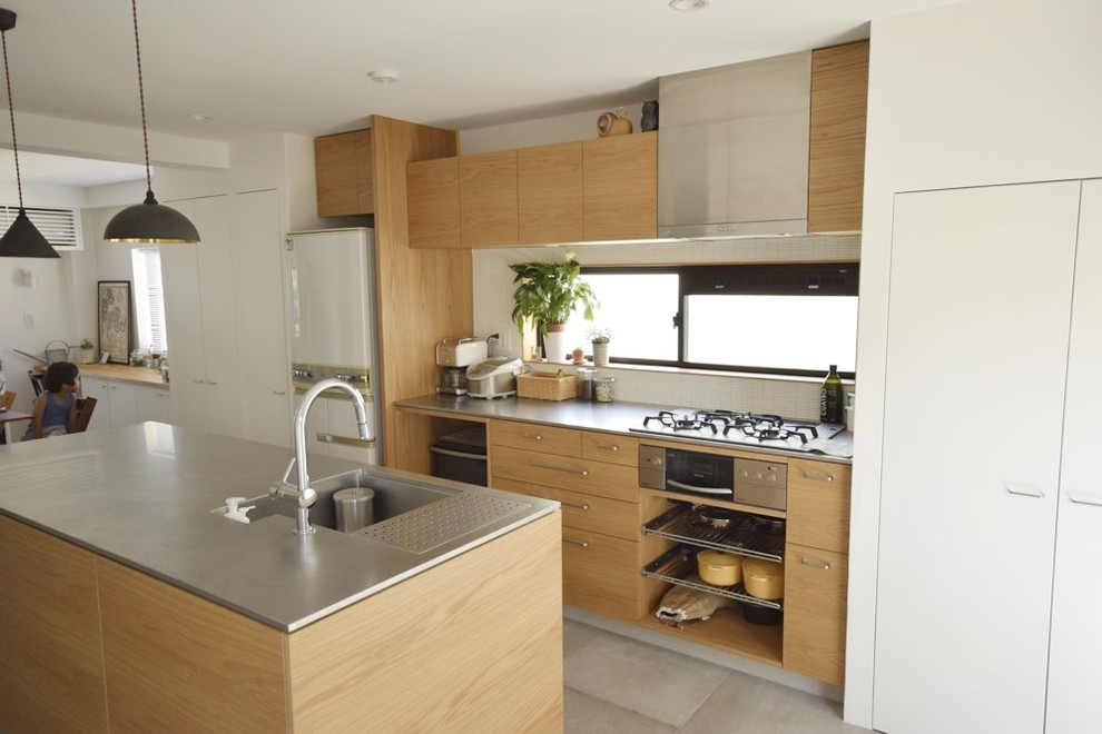 Inspiration for a modern galley open plan kitchen in Other with an integrated sink, flat-panel cabinets, light wood cabinets, stainless steel benchtops, white splashback, stainless steel appliances, concrete floors and with island.