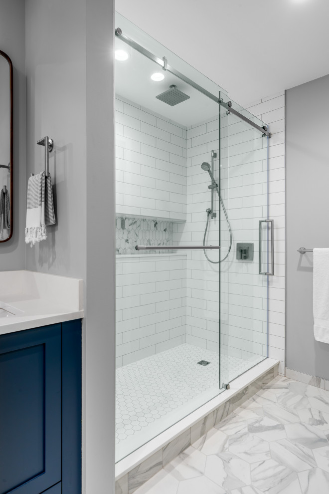 Photo of a mid-sized transitional master bathroom in Vancouver with shaker cabinets, blue cabinets, a double shower, a one-piece toilet, white tile, subway tile, grey walls, porcelain floors, an undermount sink, engineered quartz benchtops, grey floor, a sliding shower screen and white benchtops.