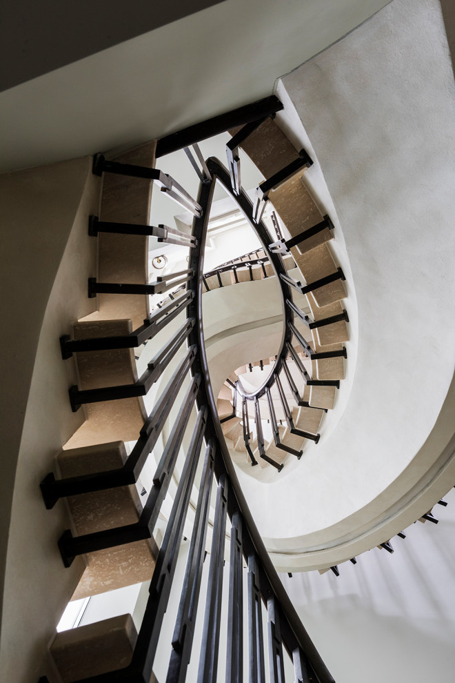 This is an example of a medium sized bohemian curved metal railing staircase in London with marble treads and concrete risers.