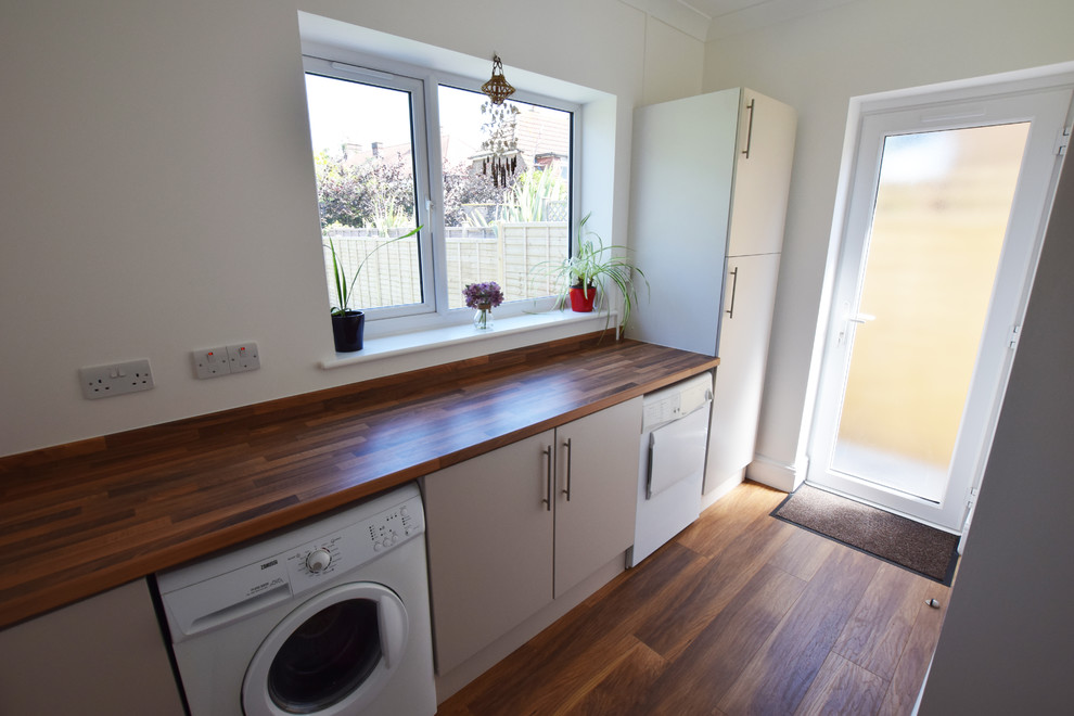 This is an example of a mid-sized traditional single-wall utility room in Sussex with a single-bowl sink, flat-panel cabinets, beige cabinets, laminate benchtops, white walls, laminate floors, an integrated washer and dryer, brown floor and brown benchtop.