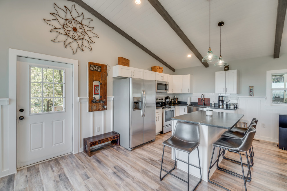 Photo of a small eclectic l-shaped eat-in kitchen in DC Metro with a farmhouse sink, shaker cabinets, white cabinets, granite benchtops, white splashback, ceramic splashback, stainless steel appliances, light hardwood floors, with island, black benchtop and timber.