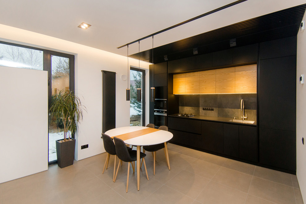 Cette image montre une cuisine linéaire design de taille moyenne avec un plan de travail en surface solide, une crédence grise, un électroménager noir et un sol en carrelage de céramique.