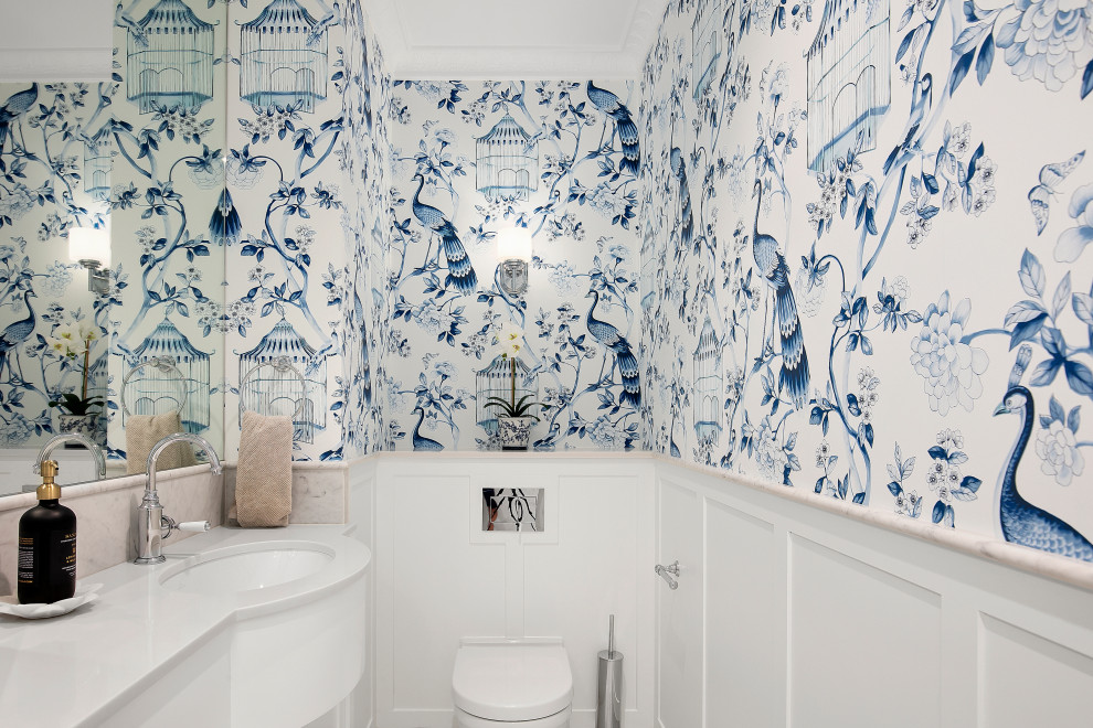 This is an example of a mid-sized beach style powder room in Sydney with white cabinets, a wall-mount toilet, marble, medium hardwood floors, an undermount sink, marble benchtops, grey benchtops, a built-in vanity and wallpaper.