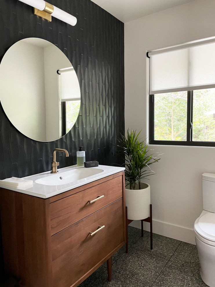 This is an example of a mid-sized midcentury bathroom in Nashville with flat-panel cabinets, medium wood cabinets, a one-piece toilet, black tile, ceramic tile, white walls, terrazzo floors, an integrated sink, solid surface benchtops, grey floor, white benchtops, a single vanity and a freestanding vanity.