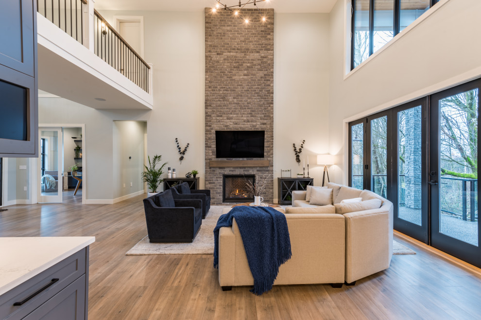 Inspiration for a large rural grey and brown open plan living room in Vancouver with white walls, laminate floors, a standard fireplace, a brick fireplace surround, a wall mounted tv, brown floors and brick walls.