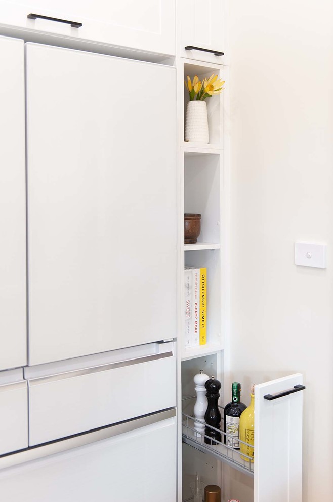 This is an example of a mid-sized modern u-shaped kitchen pantry in Melbourne with an undermount sink, shaker cabinets, white cabinets, solid surface benchtops, white splashback, porcelain splashback, white appliances, medium hardwood floors, with island and white benchtop.