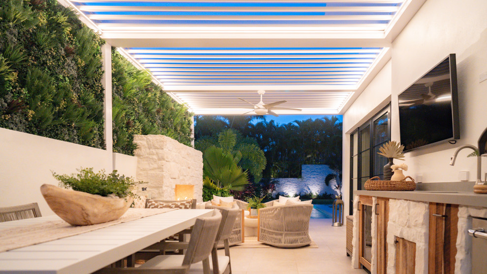 Photo of a mid-sized tropical backyard patio in Miami with natural stone pavers and a pergola.