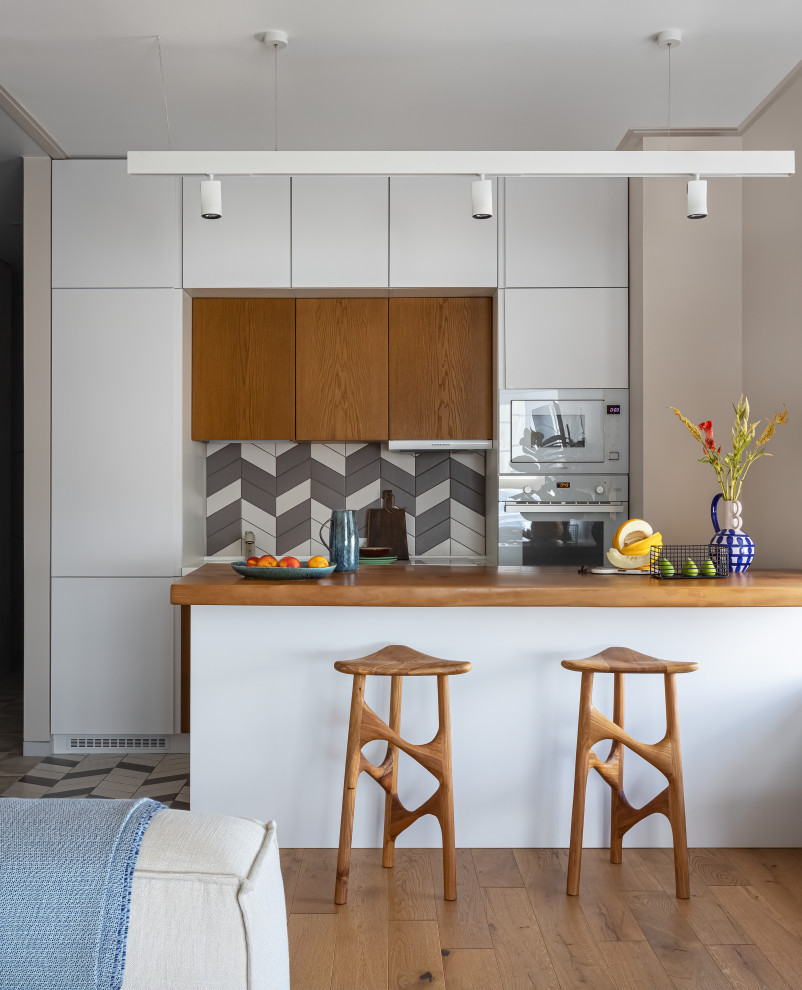 Идея дизайна: прямая кухня-гостиная в современном стиле с плоскими фасадами, белыми фасадами, разноцветным фартуком, белой техникой, полуостровом, коричневой столешницей и двухцветным гарнитуром