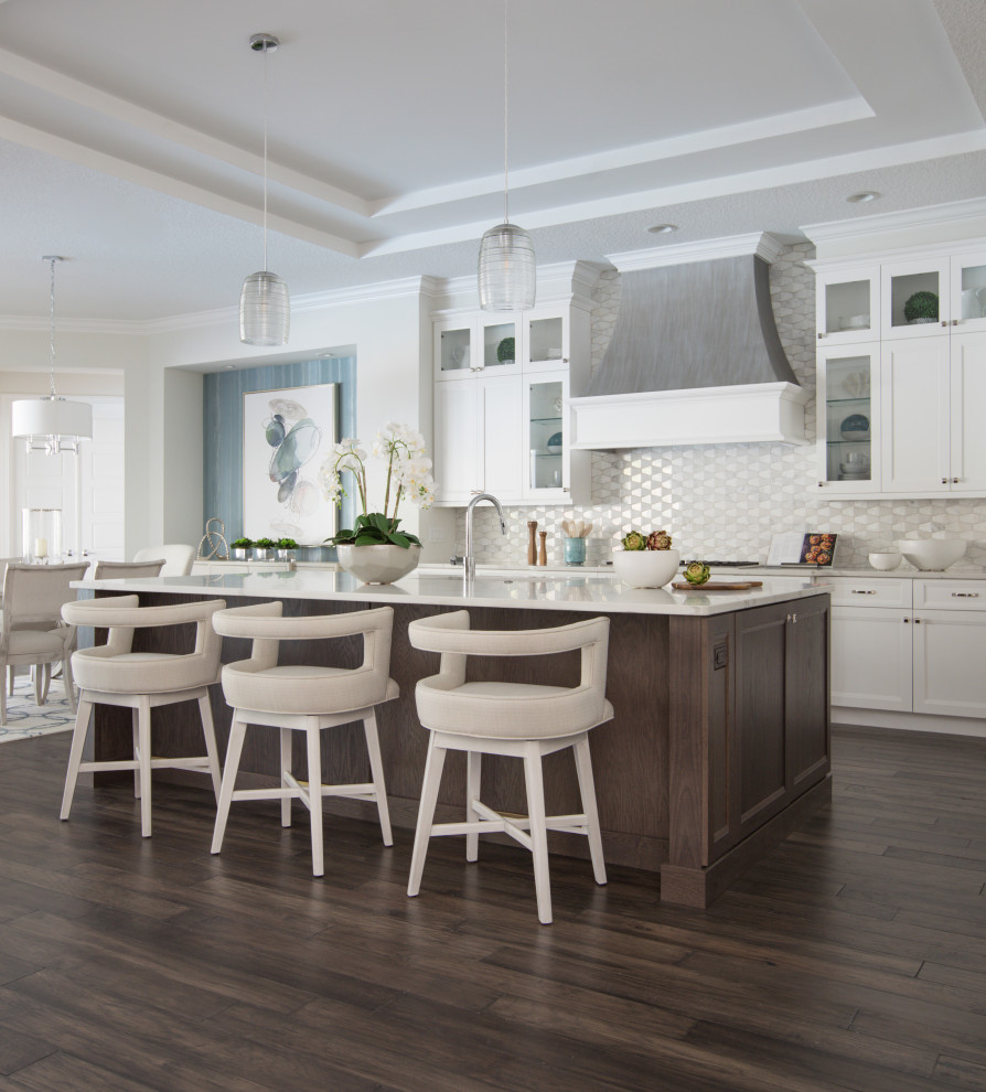 This is an example of a transitional galley kitchen in Jacksonville with shaker cabinets, white cabinets, white splashback, dark hardwood floors, with island, brown floor, white benchtop and recessed.