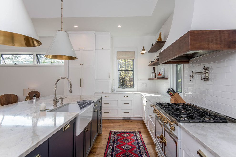 Inspiration for a country l-shaped kitchen in Other with a farmhouse sink, shaker cabinets, white cabinets, white splashback, subway tile splashback, white appliances, medium hardwood floors, with island, brown floor and grey benchtop.