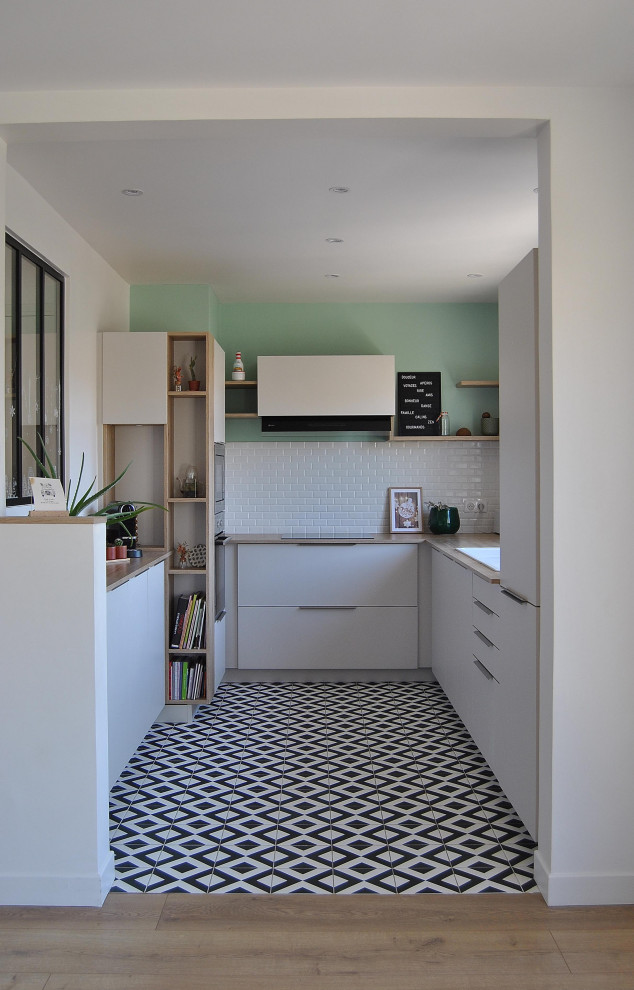 Mid-sized scandinavian u-shaped open plan kitchen in Paris with a double-bowl sink, beaded inset cabinets, white cabinets, laminate benchtops, white splashback, subway tile splashback, stainless steel appliances, ceramic floors and black floor.