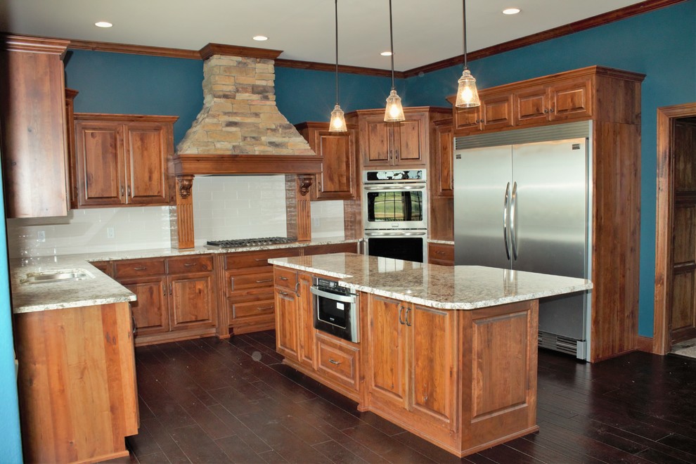 Example of a mountain style u-shaped dark wood floor eat-in kitchen design with raised-panel cabinets, dark wood cabinets, granite countertops, white backsplash, subway tile backsplash, stainless steel appliances and an island