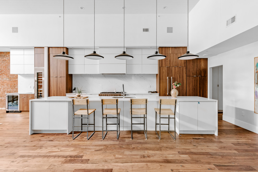 Industrial galley open plan kitchen in Denver with an undermount sink, flat-panel cabinets, medium wood cabinets, white splashback, stone slab splashback, panelled appliances, medium hardwood floors, with island, brown floor, white benchtop and timber.