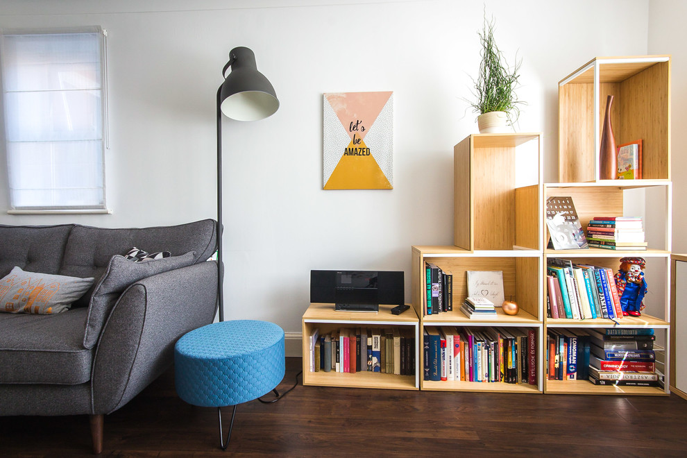 Photo of a mid-sized scandinavian enclosed living room in Berkshire with a library, white walls, laminate floors, a wall-mounted tv and brown floor.