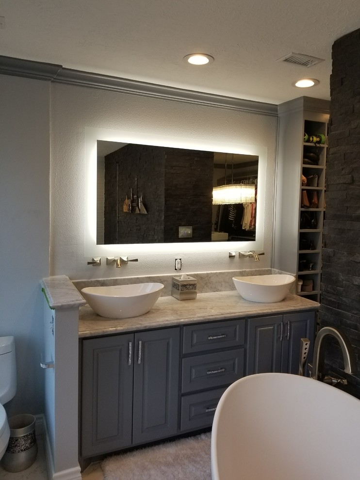 Large traditional master bathroom in Houston with shaker cabinets, grey cabinets, a freestanding tub, a double shower, an urinal, gray tile, marble, grey walls, marble floors, a vessel sink, marble benchtops, white floor and a hinged shower door.