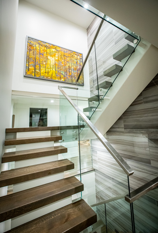 На фото: огромная лестница на больцах в современном стиле с деревянными ступенями и стеклянными перилами