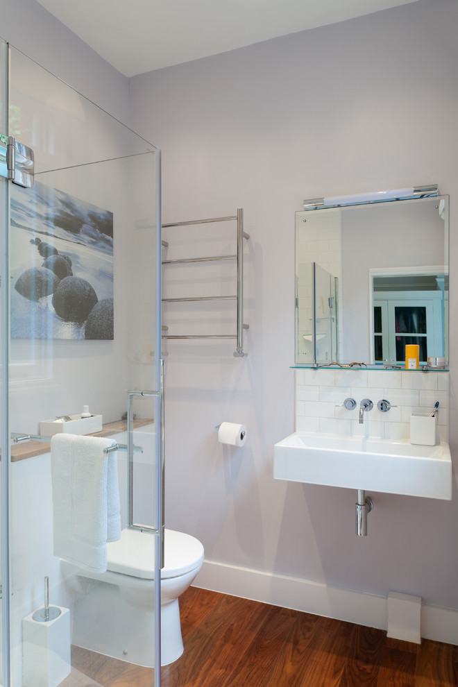 Photo of a mid-sized contemporary 3/4 bathroom in London with a wall-mount sink, a one-piece toilet, white tile, subway tile, grey walls and medium hardwood floors.