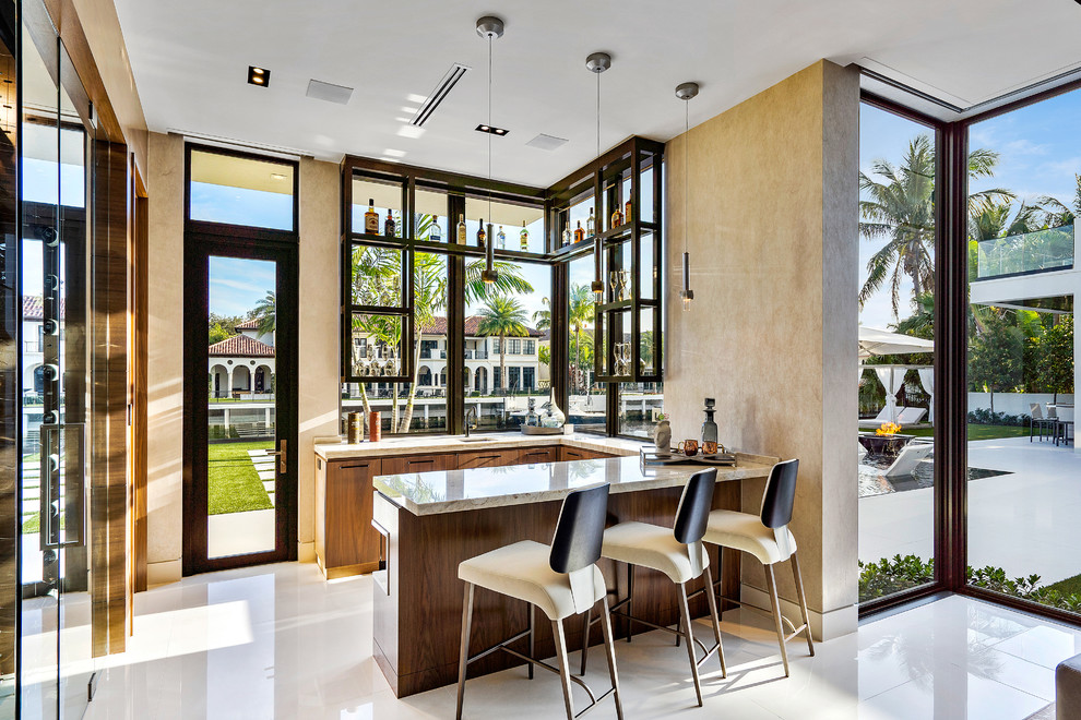 This is an example of a mid-sized contemporary u-shaped seated home bar in Miami with onyx benchtops, marble floors, white floor, beige benchtop, flat-panel cabinets and medium wood cabinets.