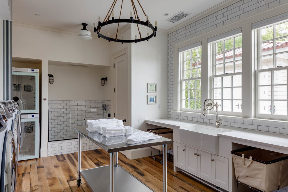 Beach style u-shaped utility room in Boston with a farmhouse sink, shaker cabinets, white cabinets, white walls, medium hardwood floors, a side-by-side washer and dryer, brown floor and white benchtop.