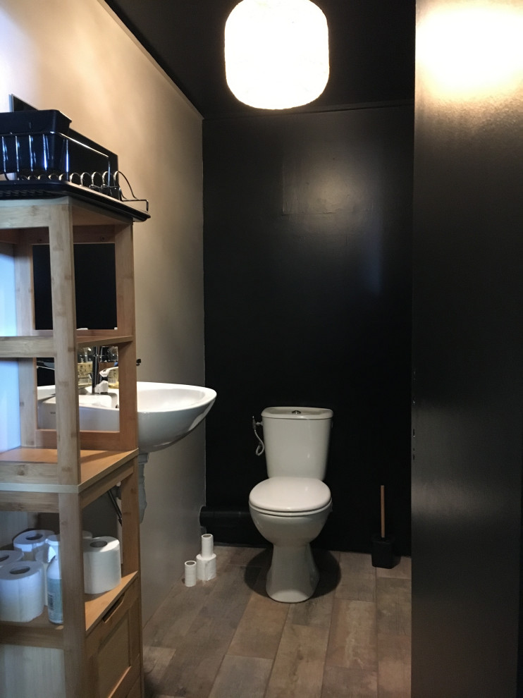 Foto på ett litet funkis toalett, med en toalettstol med hel cisternkåpa, svarta väggar, ett undermonterad handfat och brunt golv