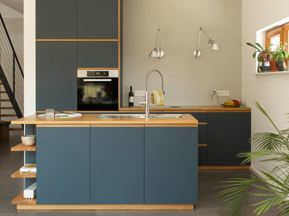 Modern inredning av ett mellanstort brun brunt kök, med en nedsänkt diskho, släta luckor, blå skåp, träbänkskiva, grått stänkskydd, betonggolv, en köksö och grått golv